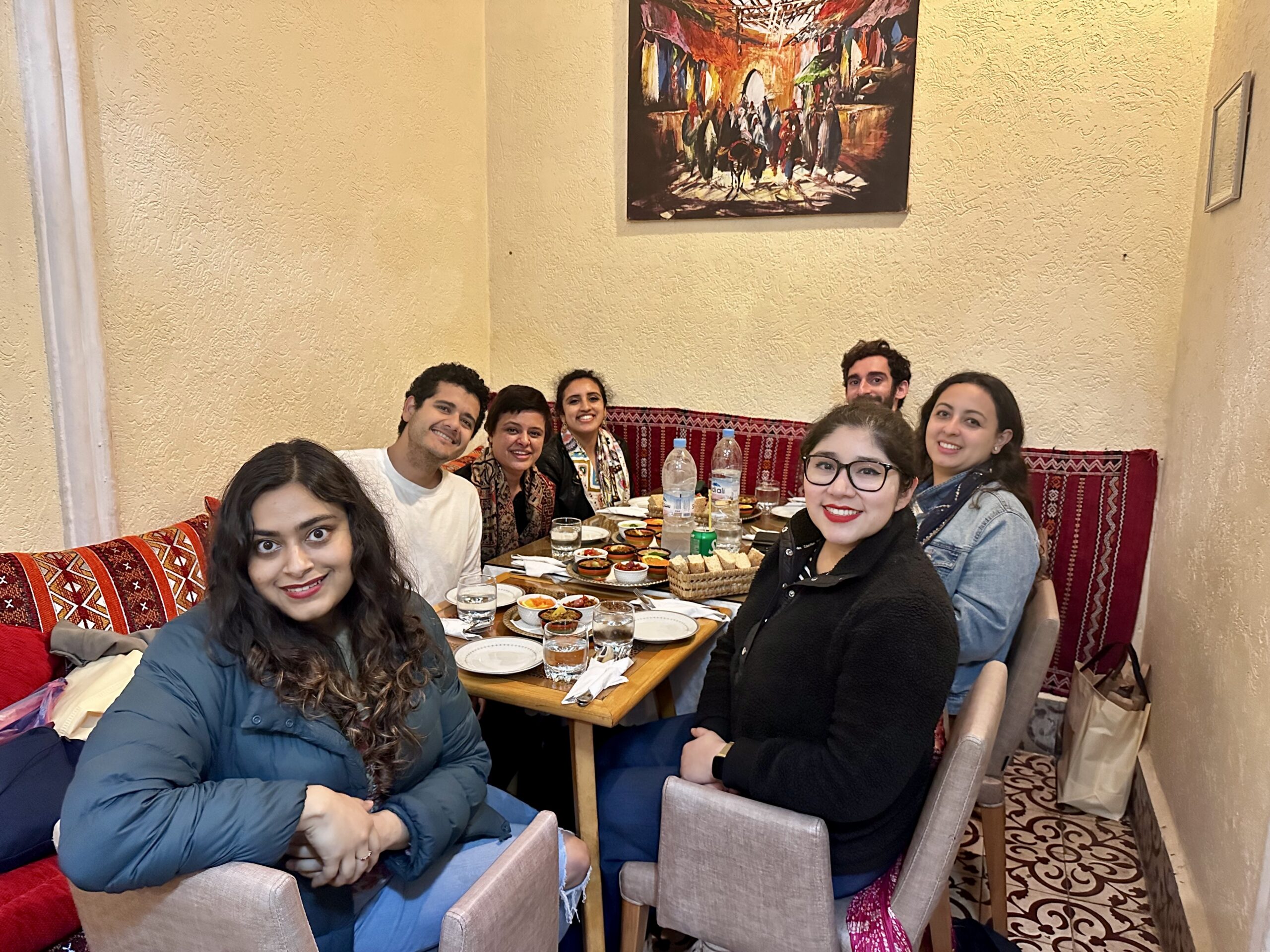 A small group of people sitting around a table in a cozy, decorated restaurant setting. They are smiling and enjoying a meal together.