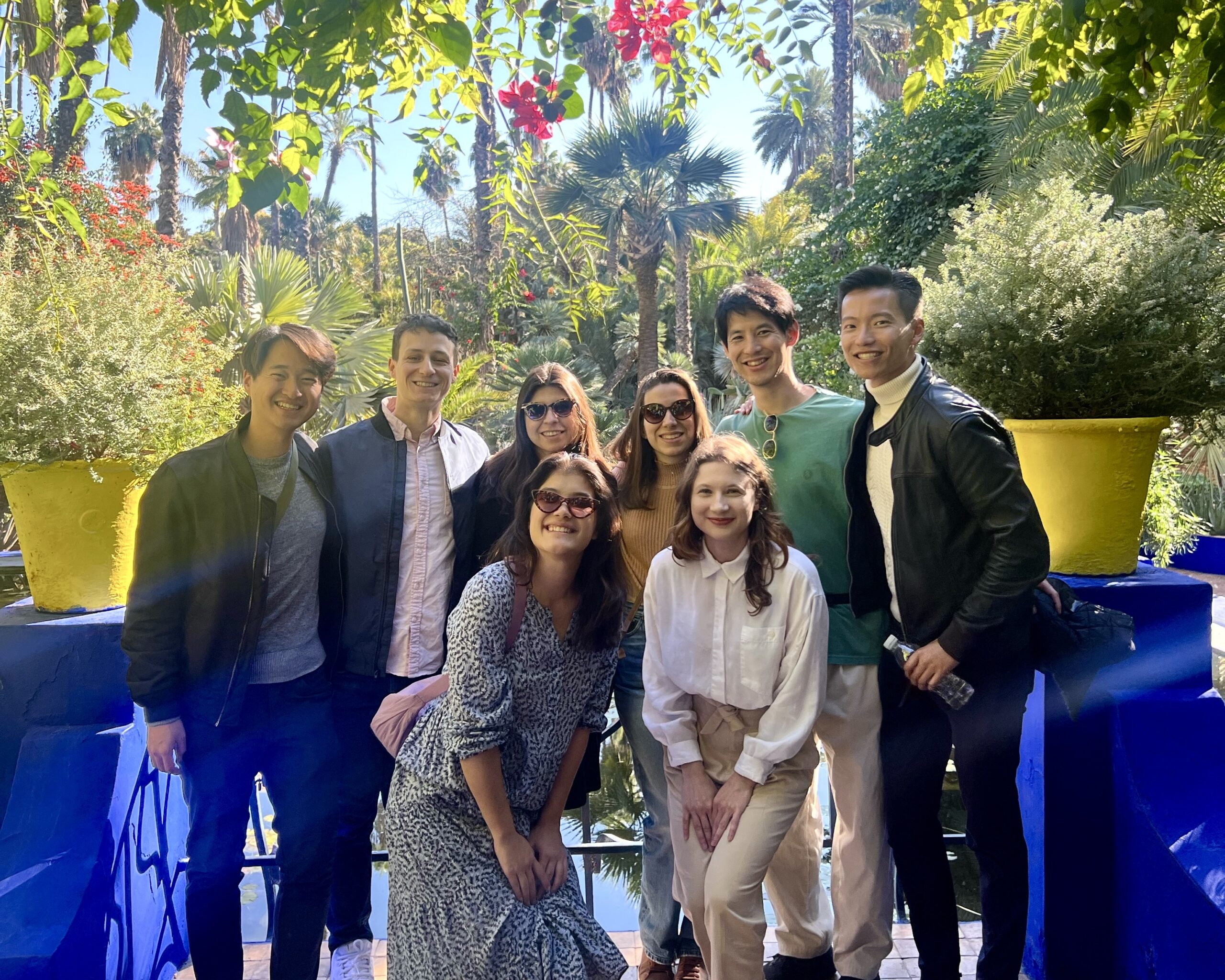 A group of people smiling and posing together in a lush garden setting, surrounded by vibrant greenery and colorful foliage.