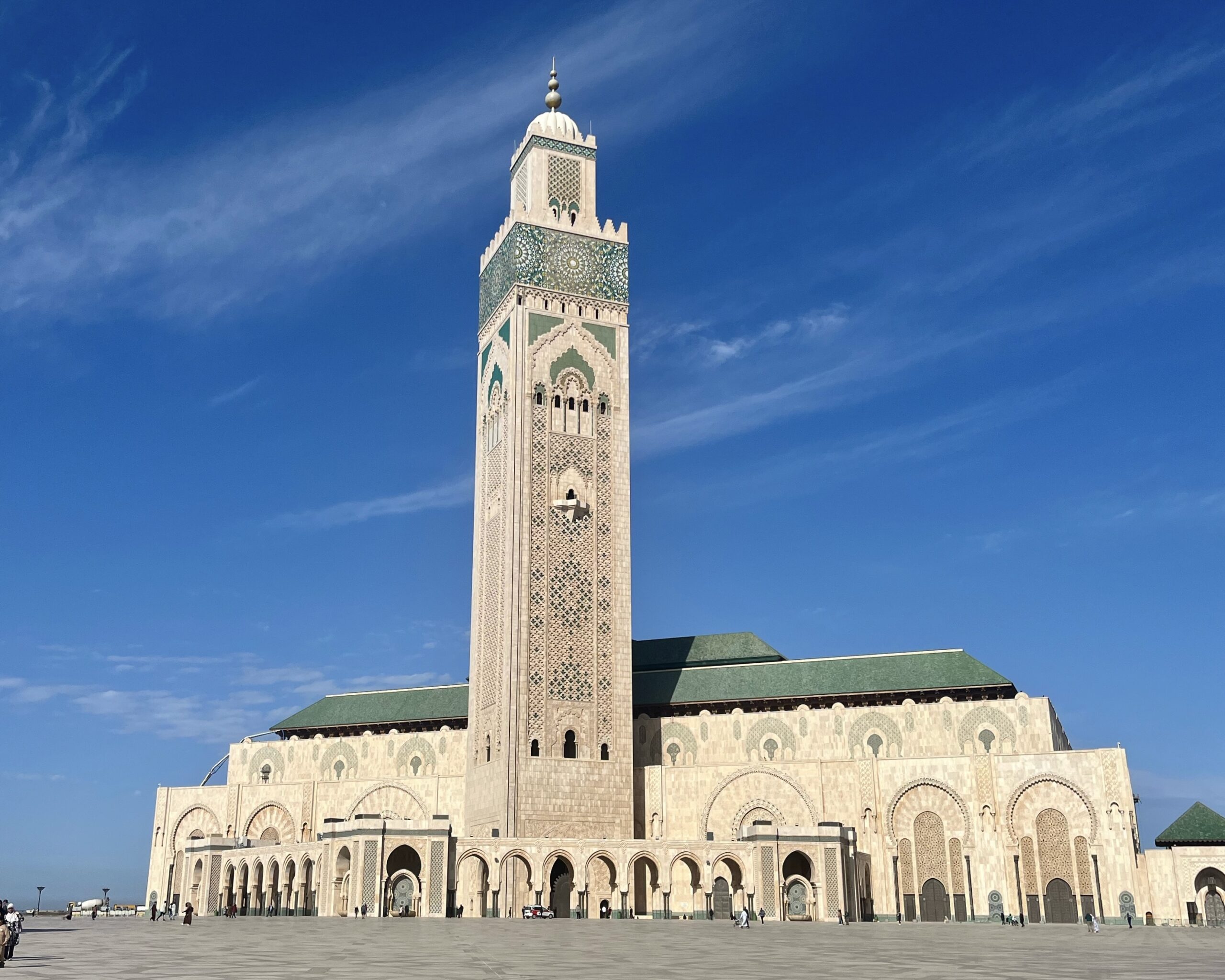 A large mosque with a tall, ornate minaret and intricate architectural details, set against a clear blue sky.