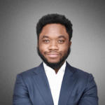 Individual in a business suit smiling with arms crossed, set against a neutral gray background.
