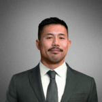 Headshot of person in a suit and tie against a gray background.