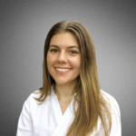 A person with long hair is smiling and wearing a white shirt against a neutral gray background.