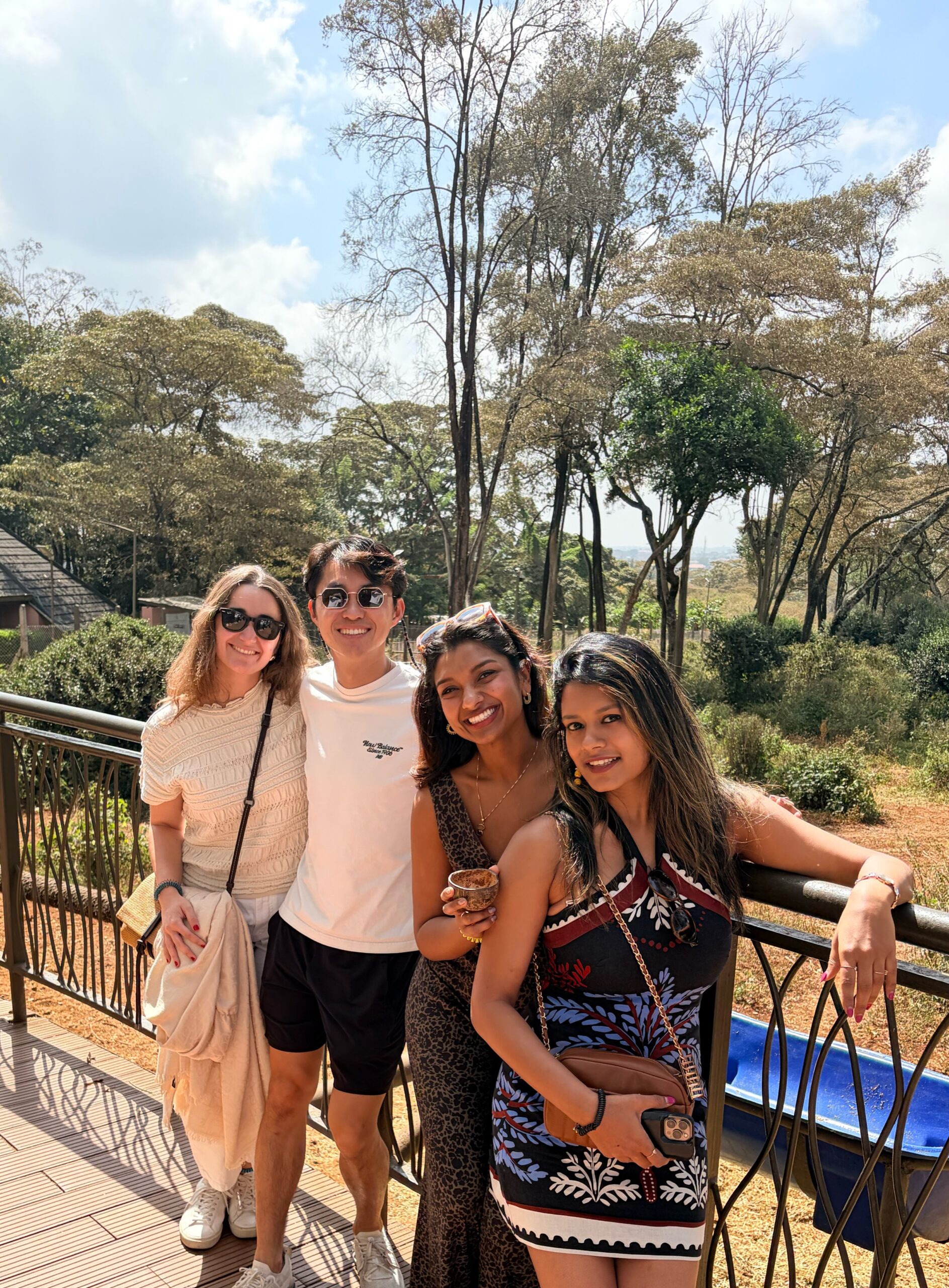 Culture Quest Kenya (1) Several people smiling and posing outdoors in a sunny setting with trees and a fence in the background.