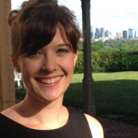 Headshot of a person smiling with a cityscape in the background on a sunny day.